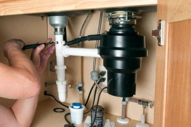 Plumber repairing a garbage disposal beneath a kitchen sink in Wesley Chapel